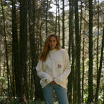 Woman subtly lifts up the bottom of sweater amidst a backdrop of tall trees