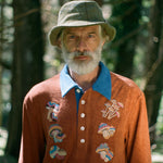 older male model in a forest wearing the Tombolo embroidered mushroom classic long sleeve organic cotton terry cloth shirt with a fun disco vibe