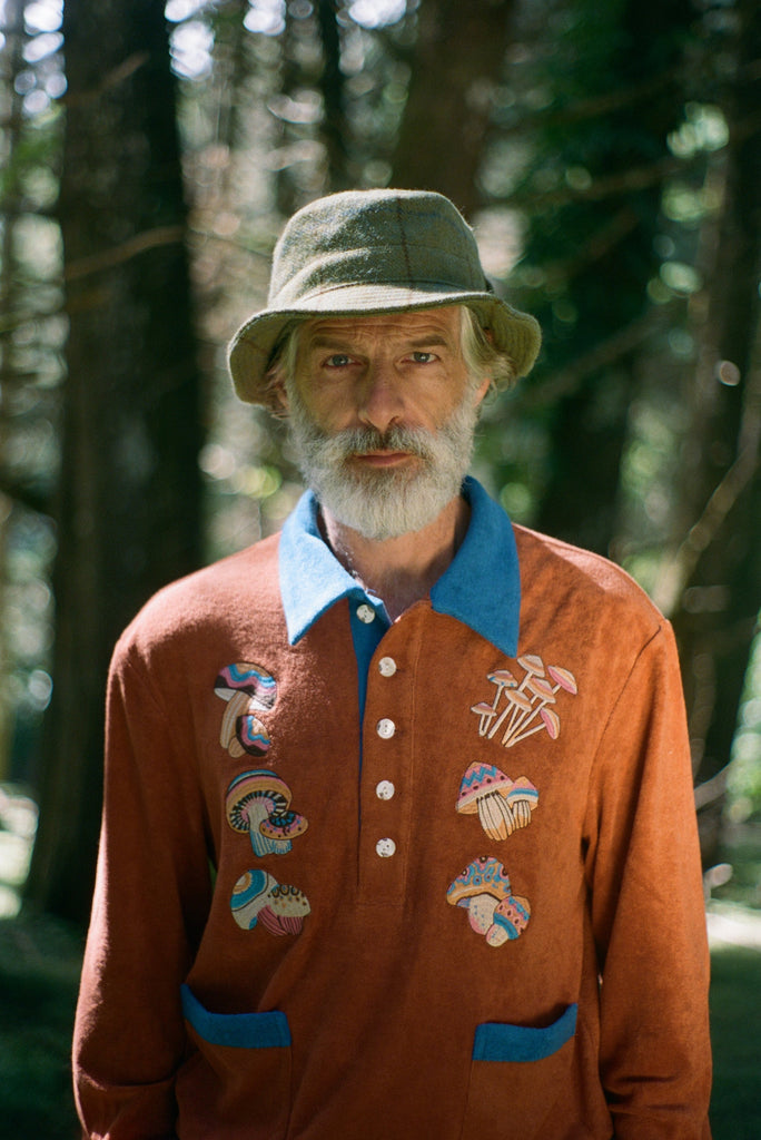 older male model in a forest wearing the Tombolo embroidered mushroom classic long sleeve organic cotton terry cloth shirt with a fun disco vibe