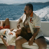 Two people relaxing on a moving boat with ocean and island views in the background, both wearing the 'Crouching Tiger" Cabana Shirt.