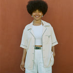 female model wearing cabrisa unbuttoned with white pants and a green belt