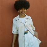 Female model wearing shirt with one button buttoned leaning on wall