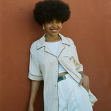 Female model wearing shirt with one button buttoned leaning on wall