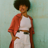Female model leaning on wall with cabrisa shirt unbuttoned over an all white outfit