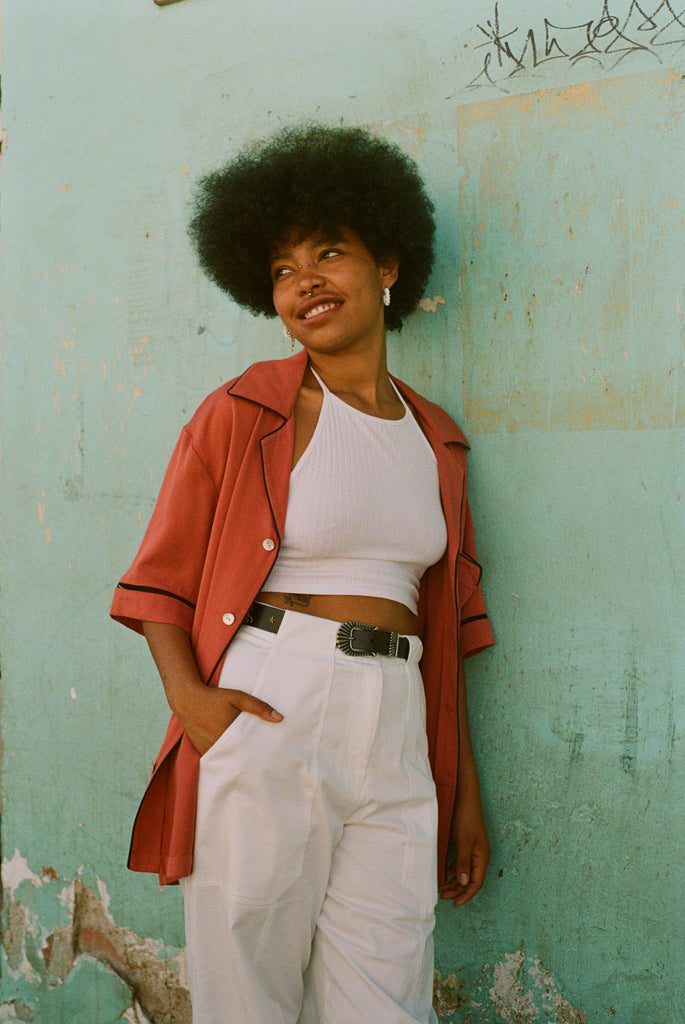 Female model leaning on wall with cabrisa shirt unbuttoned over an all white outfit