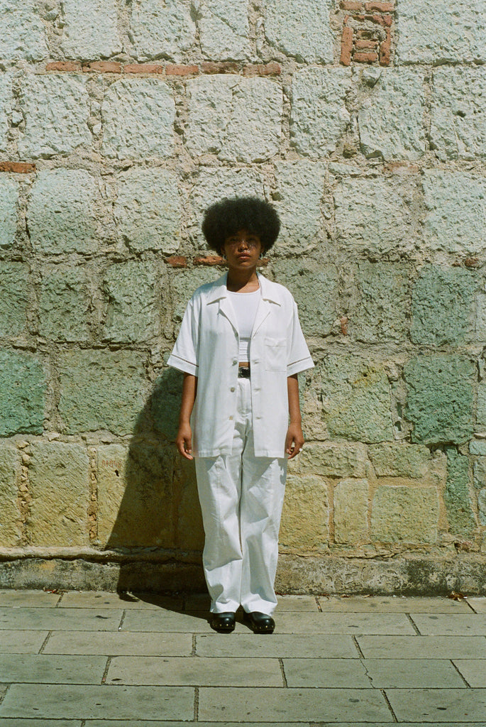 Female model wearing shirt over an all-white outfit standing against a wall