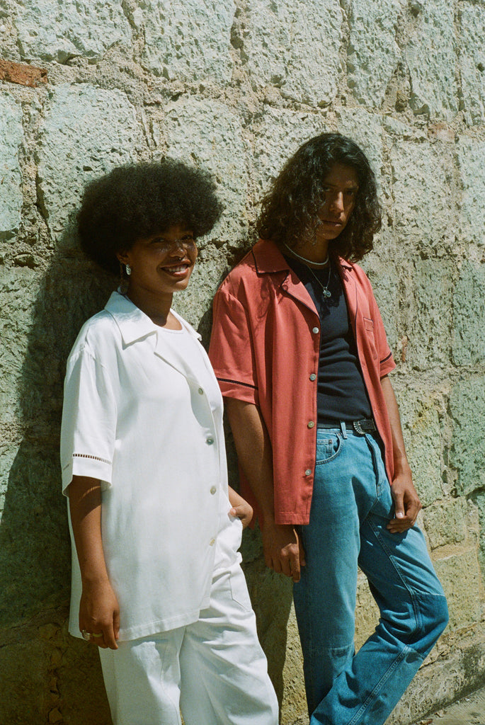 Female and male model leaning against wall looking left at camera