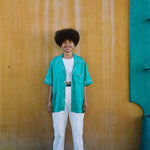 Female model wearing teal cabrisa over all white outfit standing against a wooden wall