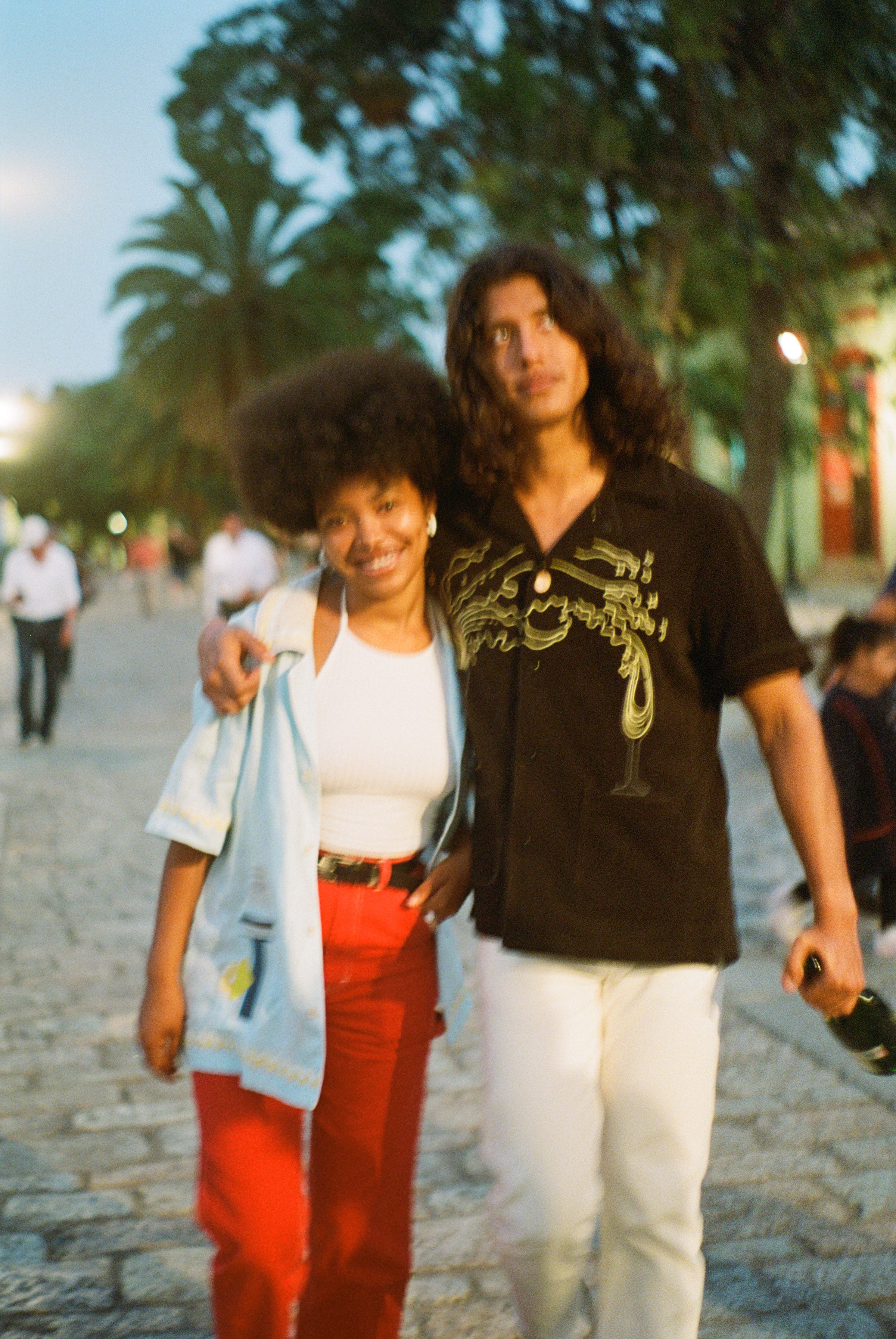 Man puts arm around woman walking through a town square while wearing Big Brut cabana shirt