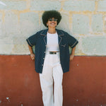 Female model wearing shirt unbuttoned over an all white outfit leaning against a wall