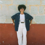 Female model wearing shirt unbuttoned over an all white outfit leaning against a wall