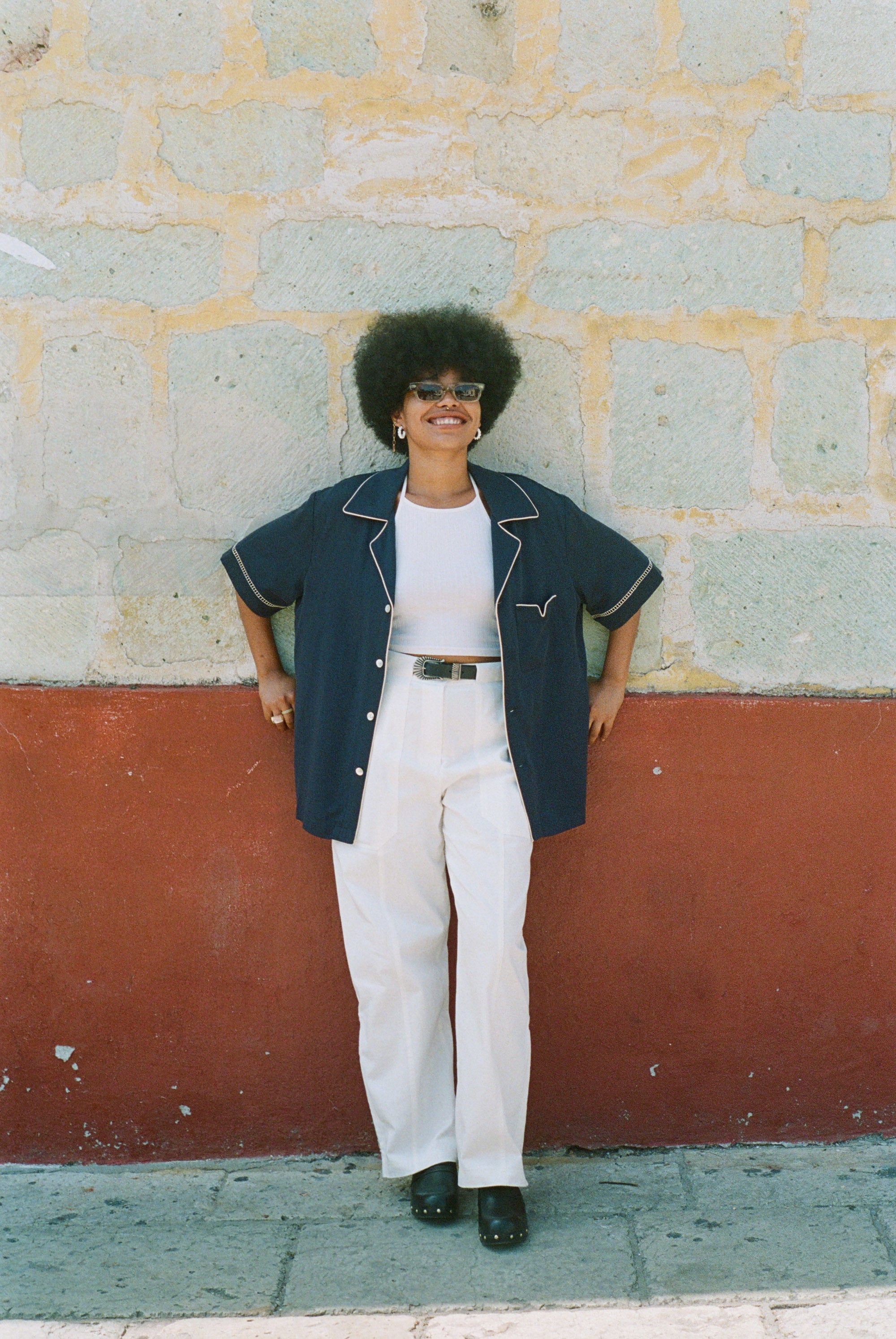 Female model wearing shirt unbuttoned over an all white outfit leaning against a wall
