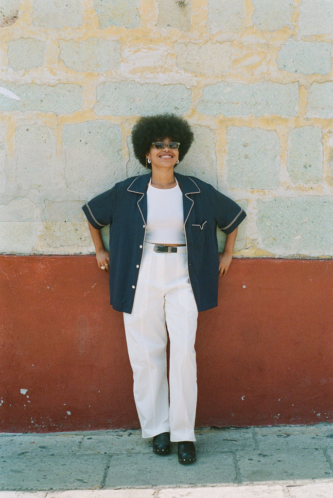 Female model wearing shirt unbuttoned over an all white outfit leaning against a wall