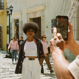 Female model wearing navy cabrisa unbuttoned on a street being photographed with an iPhone