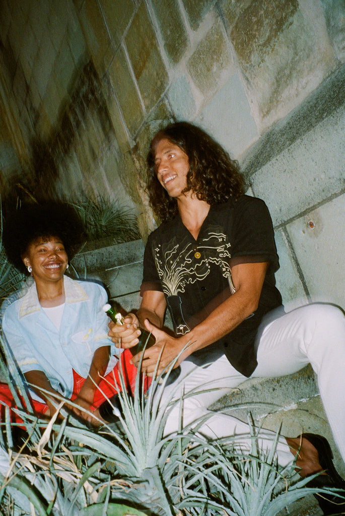 Man and woman sit on bench as man pops champagne bottle
