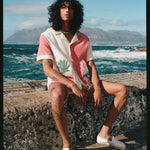 Male model sitting on a ledge by the sea wearing the full Gusanito set