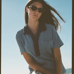 Female model posing in blue polo on beach with sunglasses