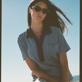 Female model posing in blue polo on beach with sunglasses