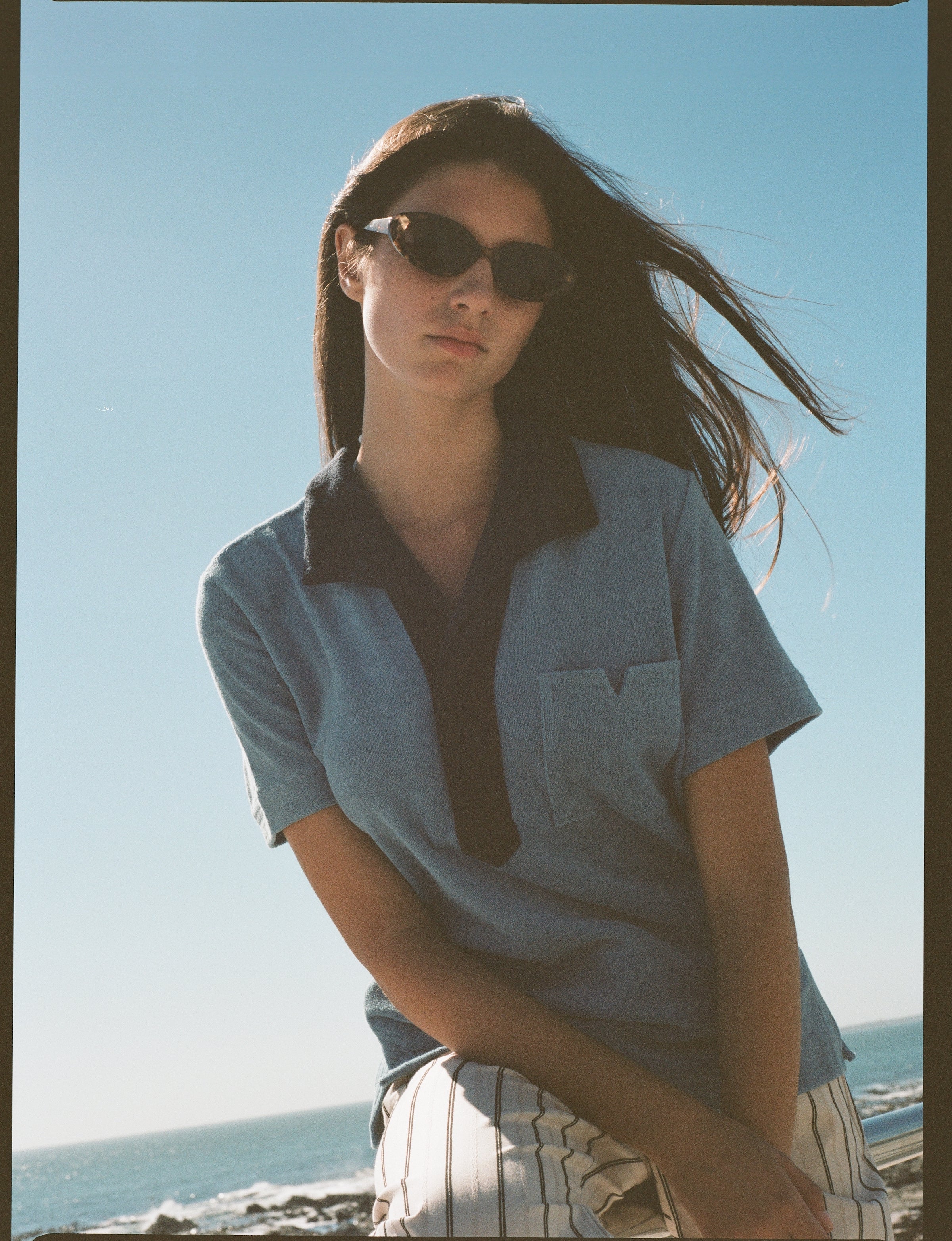 Female model posing in blue polo on beach with sunglasses