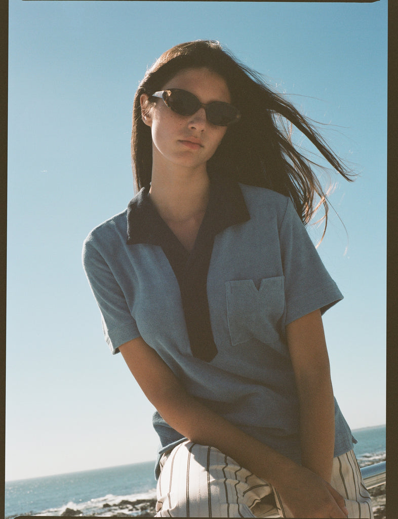 Female model posing in blue polo on beach with sunglasses