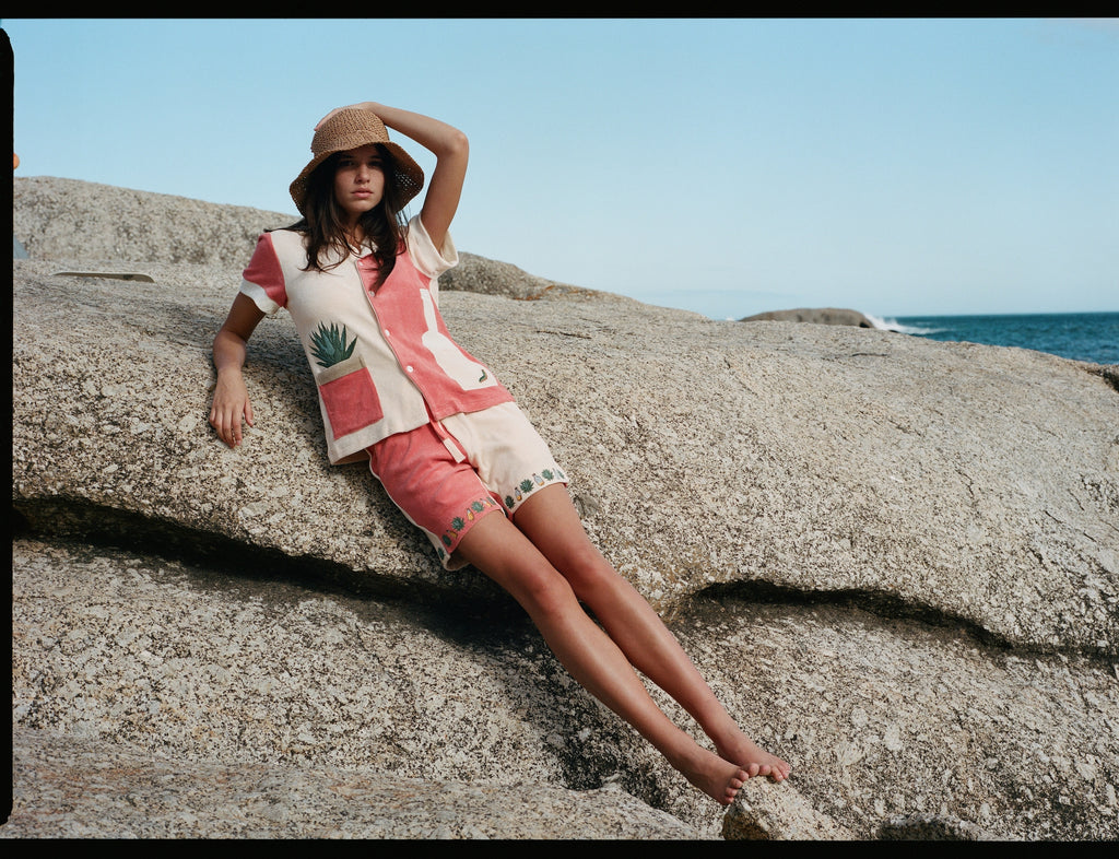 Female model leaning on a rock wearing the full terry cloth Gusanito set along with a woven sun hat