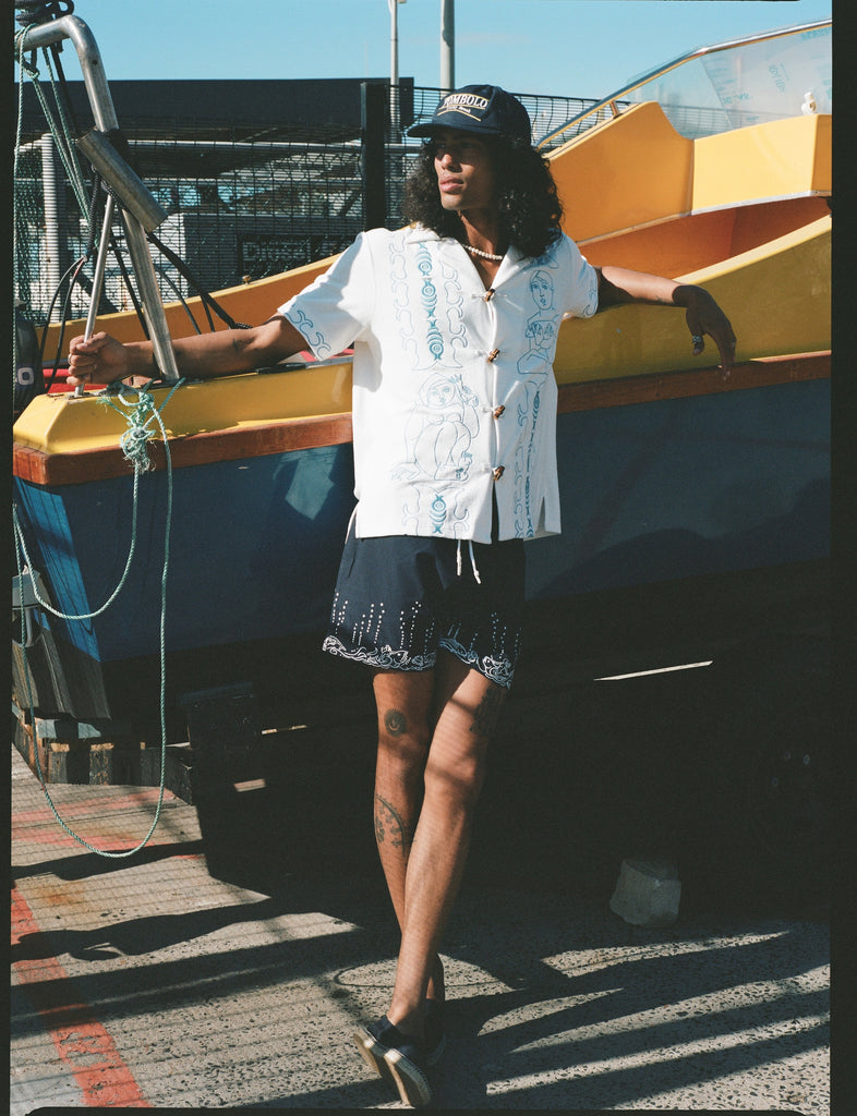 male model relaxing against a boat in his fruits de mer swim trunks