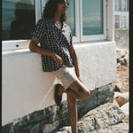 Male model leaning against windows and wall in shirt and shorts