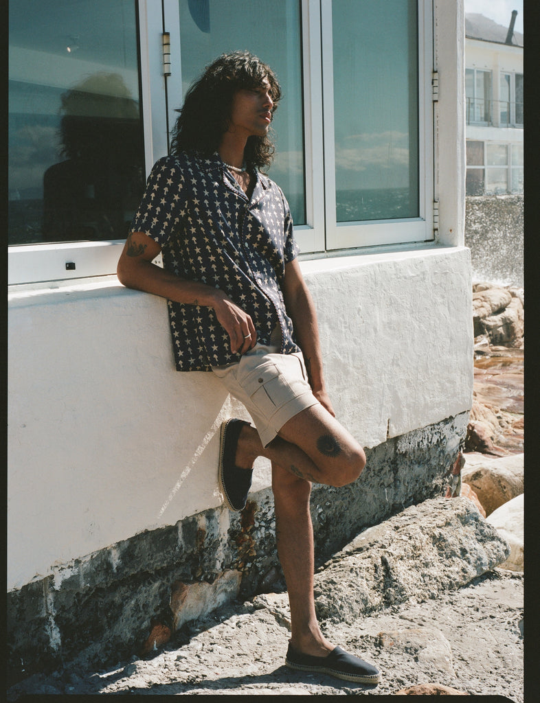 Male model leaning against windows and wall in shirt and shorts