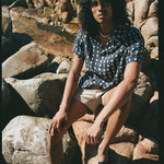 Male model wearing previous outfit sitting on a rocky beach