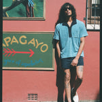Male model leaning on pink wall wearing blue polo