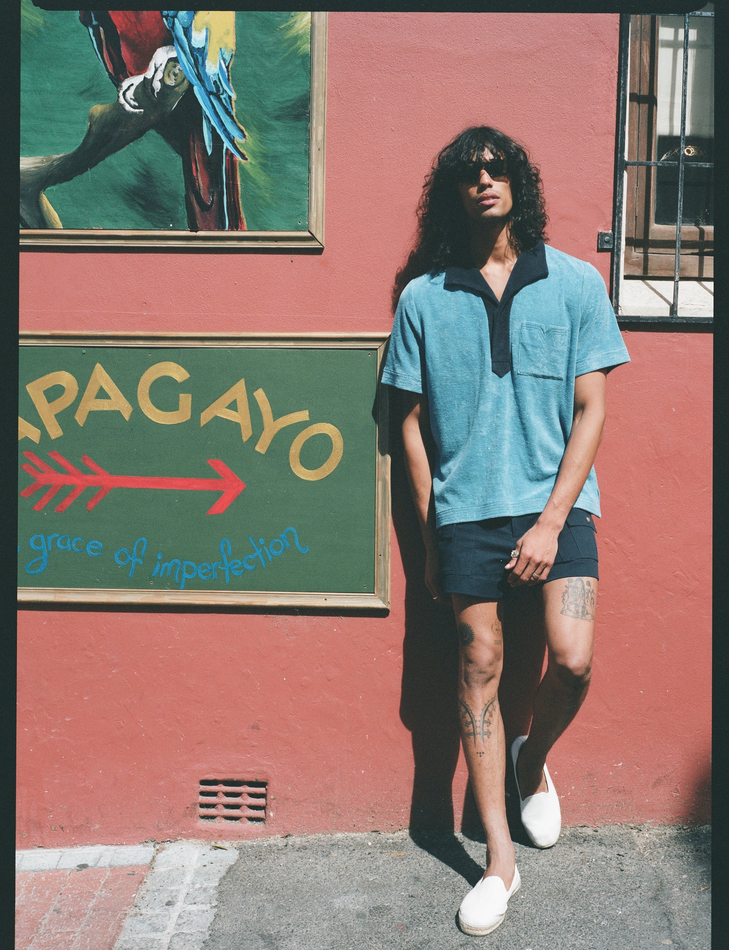 Male model leaning on pink wall wearing blue polo
