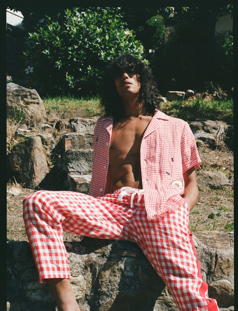man with unbuttoned shirt sits on rock