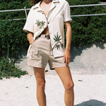 Woman closes eyes standing on beach with one hand in pocket