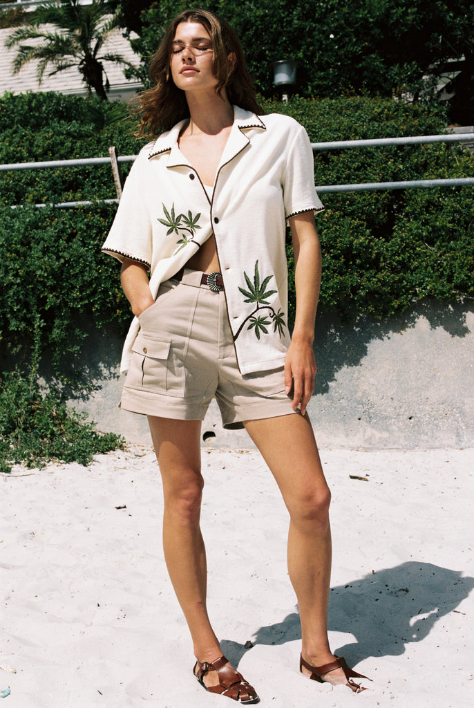 Woman closes eyes standing on beach with one hand in pocket