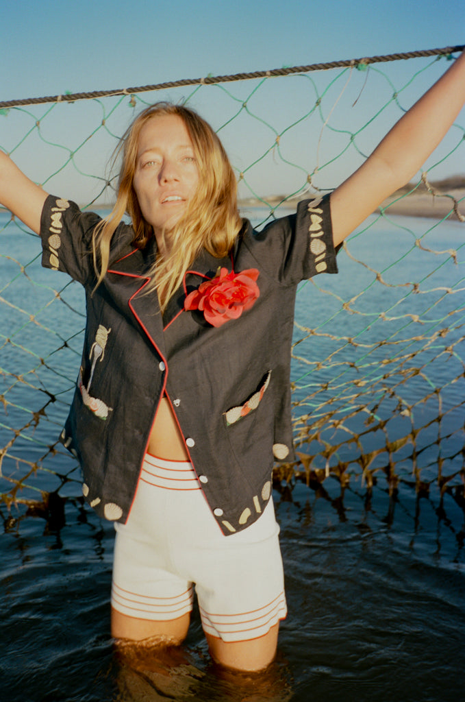 Female model wearing vongole crop holding up a fishing net in the ocean