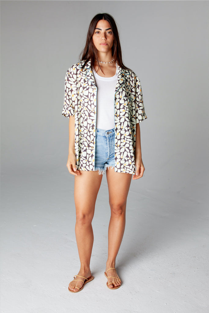 Shirt unbuttoned over a white tank top and jean shorts on a female model