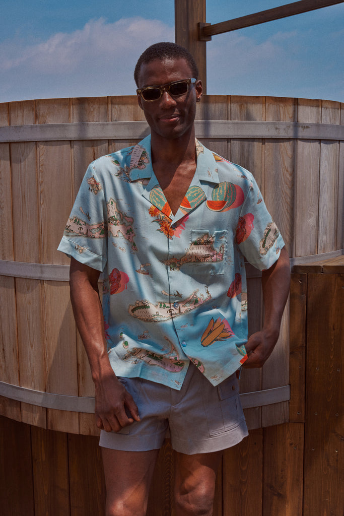 Male model wearing the top and khaki stowaway shorts leaning on fence 