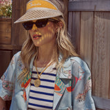 Female model in island hopper tee leaning on fence wearing visor