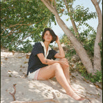 woman sits in sand and poses sideways wearing navy polo shirt