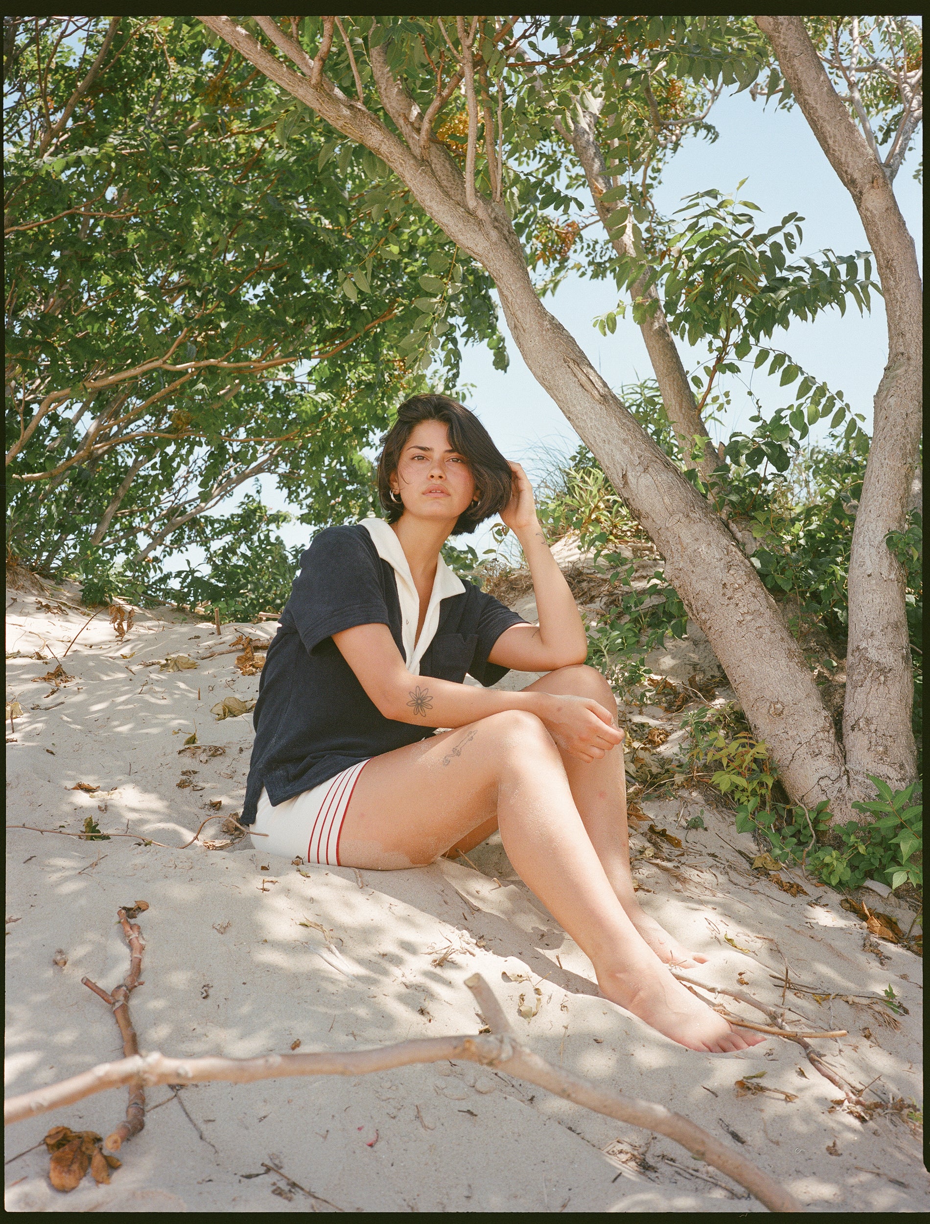 woman sits in sand and poses sideways wearing navy polo shirt