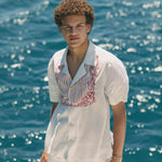 Male model on boat looking up at camera wearing shirt with white pants