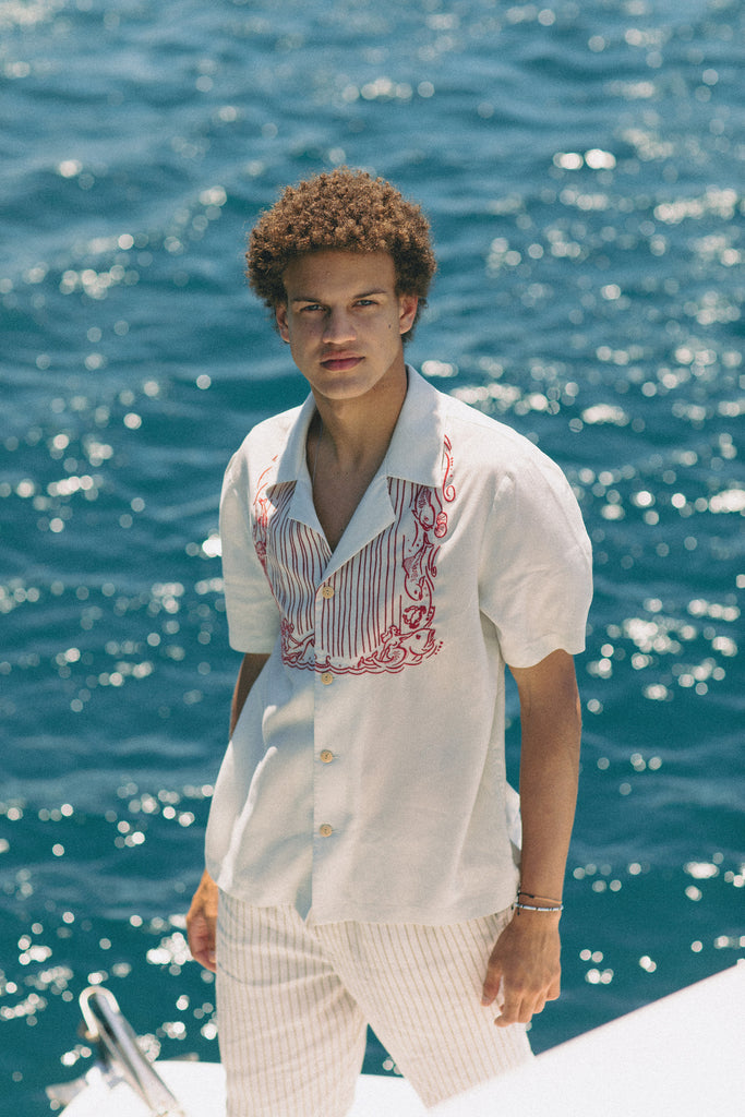 Male model on boat looking up at camera wearing shirt with white pants