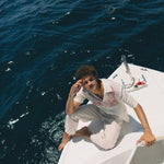 Male model sitting on edge of boat wearing shirt with white pants