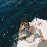 Male model sitting on edge of boat wearing shirt with white pants