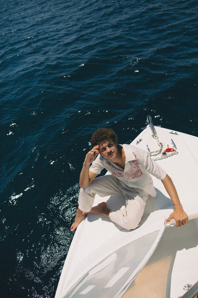 Male model sitting on edge of boat wearing shirt with white pants