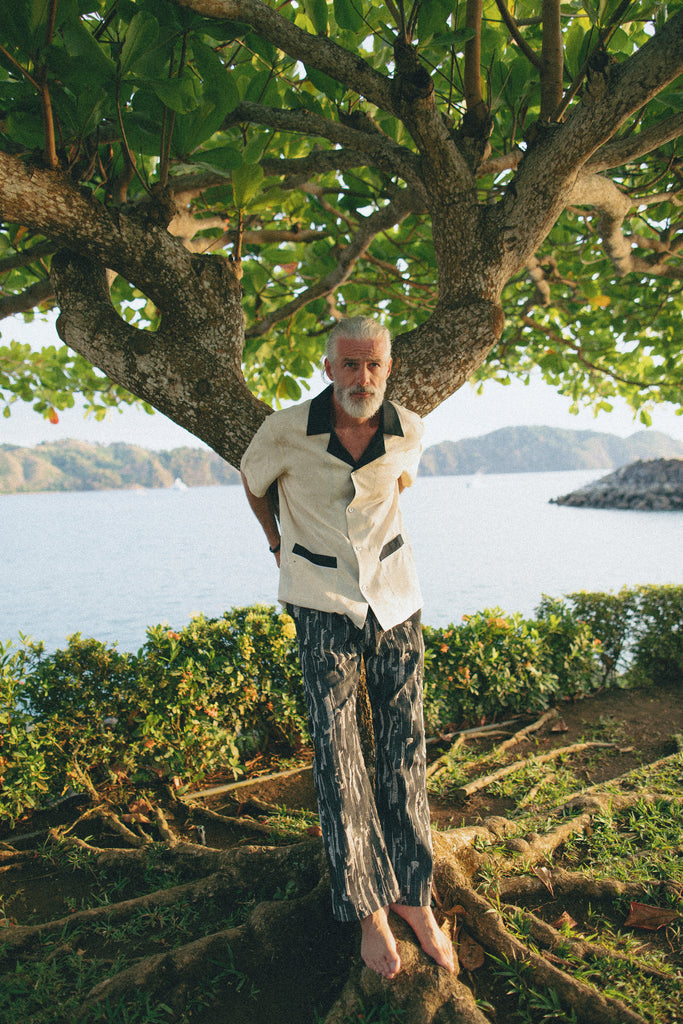 Male model wearing cabana with patterned pants leaning on tree