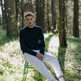 Wide shot of Man sitting in forest looking straight at camera