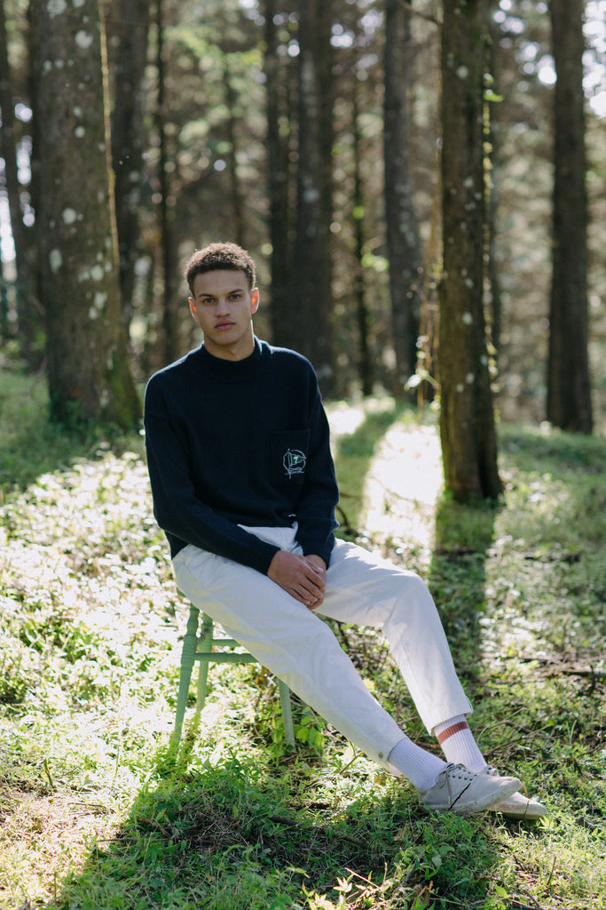 Wide shot of Man sitting in forest looking straight at camera