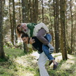 younger man carries older man and woman on his back, laughing as they all display different colors of the sweater