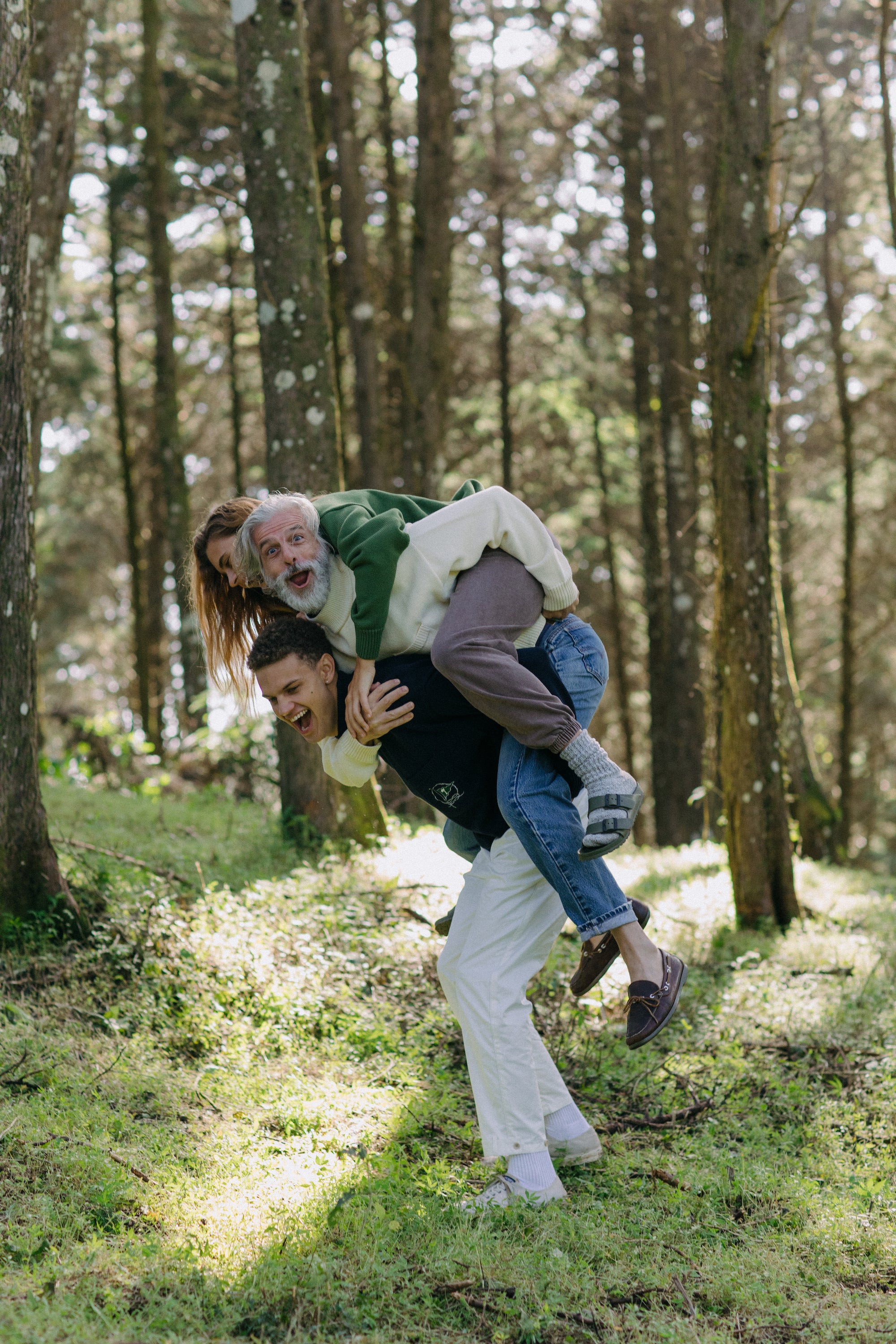 younger man carries older man and woman on his back, laughing as they all display different colors of the sweater